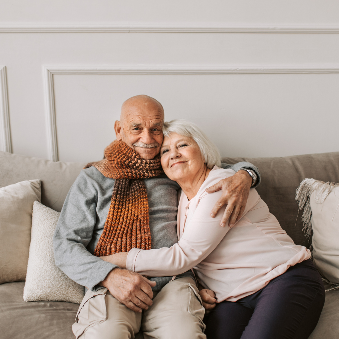 Two older people hugging on a couch comforting each other.